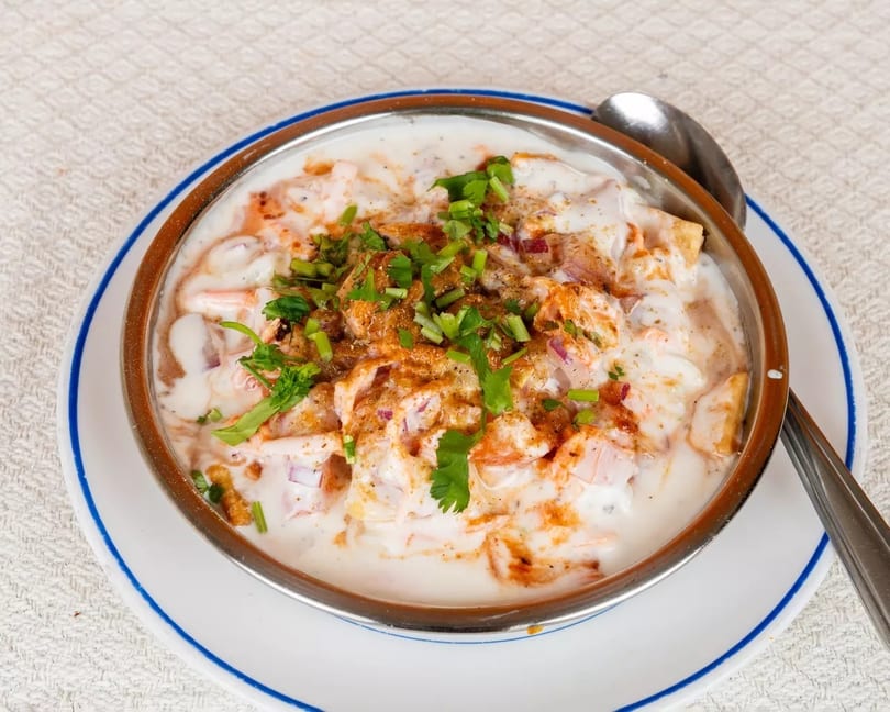 Close-up of a bowl of dahi vada, topped with red onions, spices, and fresh cilantro.