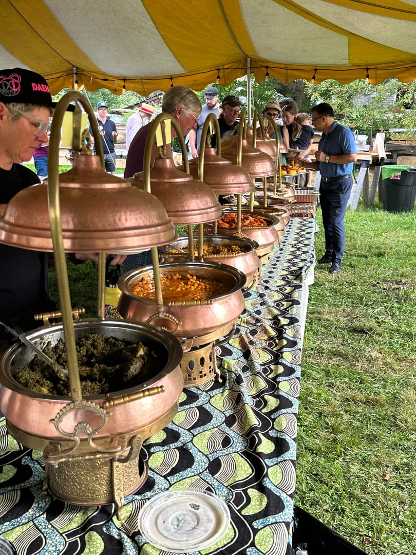 People serving themselves from a buffet line of copper chafing dishes under a striped tent.
